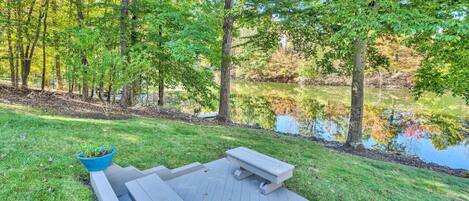 A wooden deck with benches and a planter, surrounded by trees and a body of water.