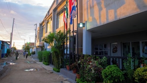 A street view with buildings, flags, and a dirt road. - HOTEL LLAELL (Luanda)