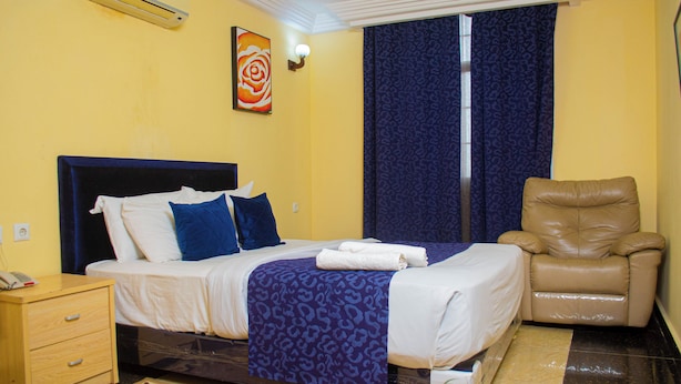 A hotel room with a bed, a chair, a nightstand, and a painting on the wall. - HOTEL LLAELL (Luanda)