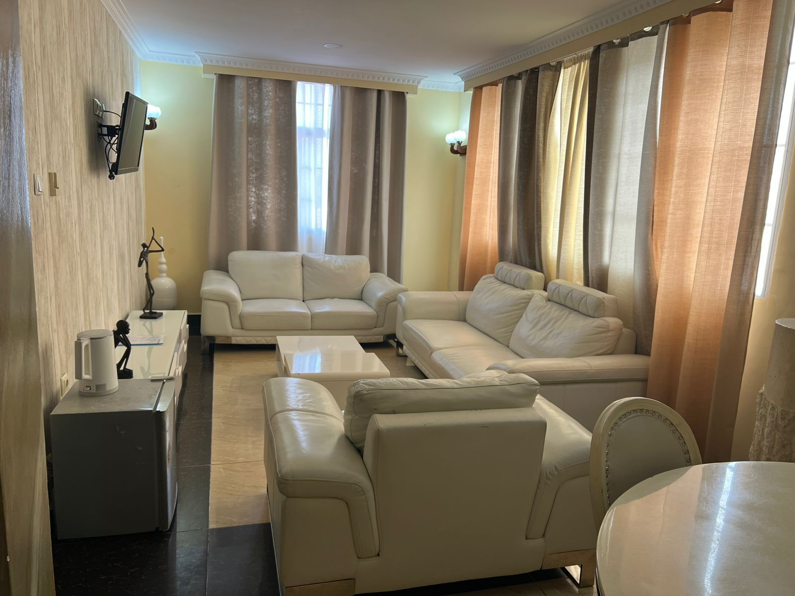 A living room with a sofa set, a coffee table, a lamp, and a television mounted on the wall.