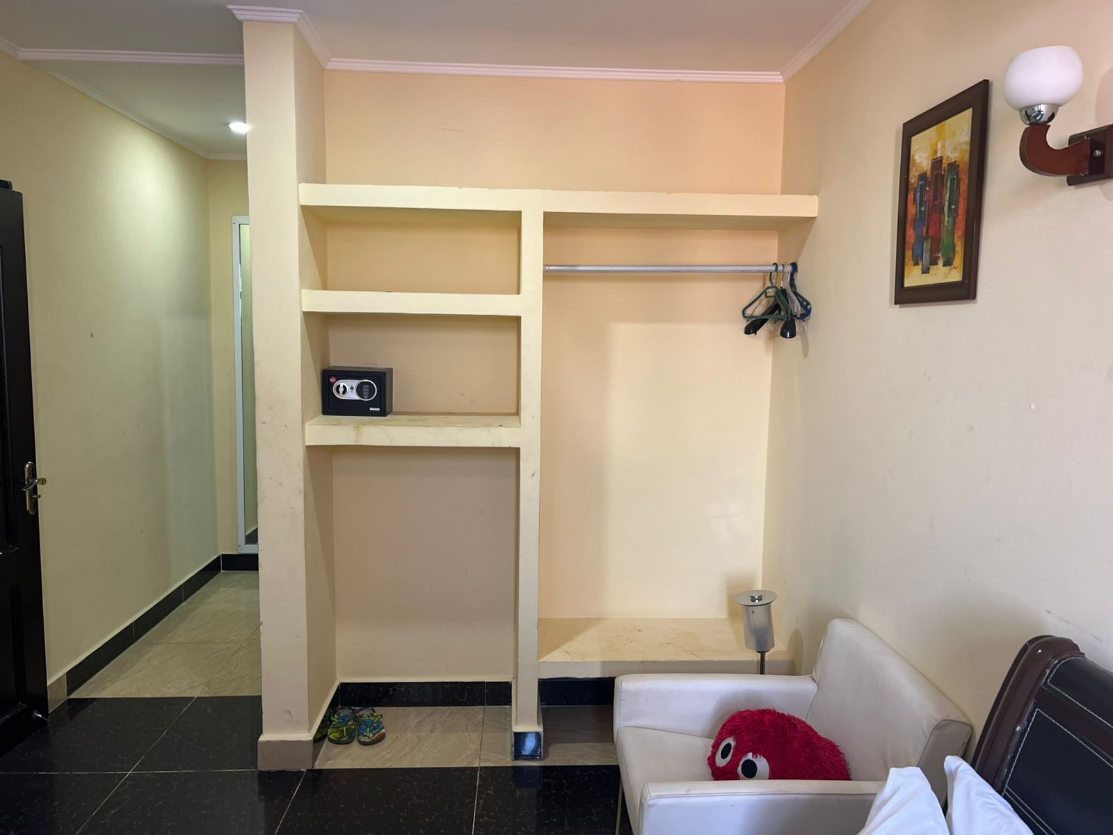 Una habitación con un sofá blanco, un peluche rojo, un estante con una radio y un cuadro en la pared.