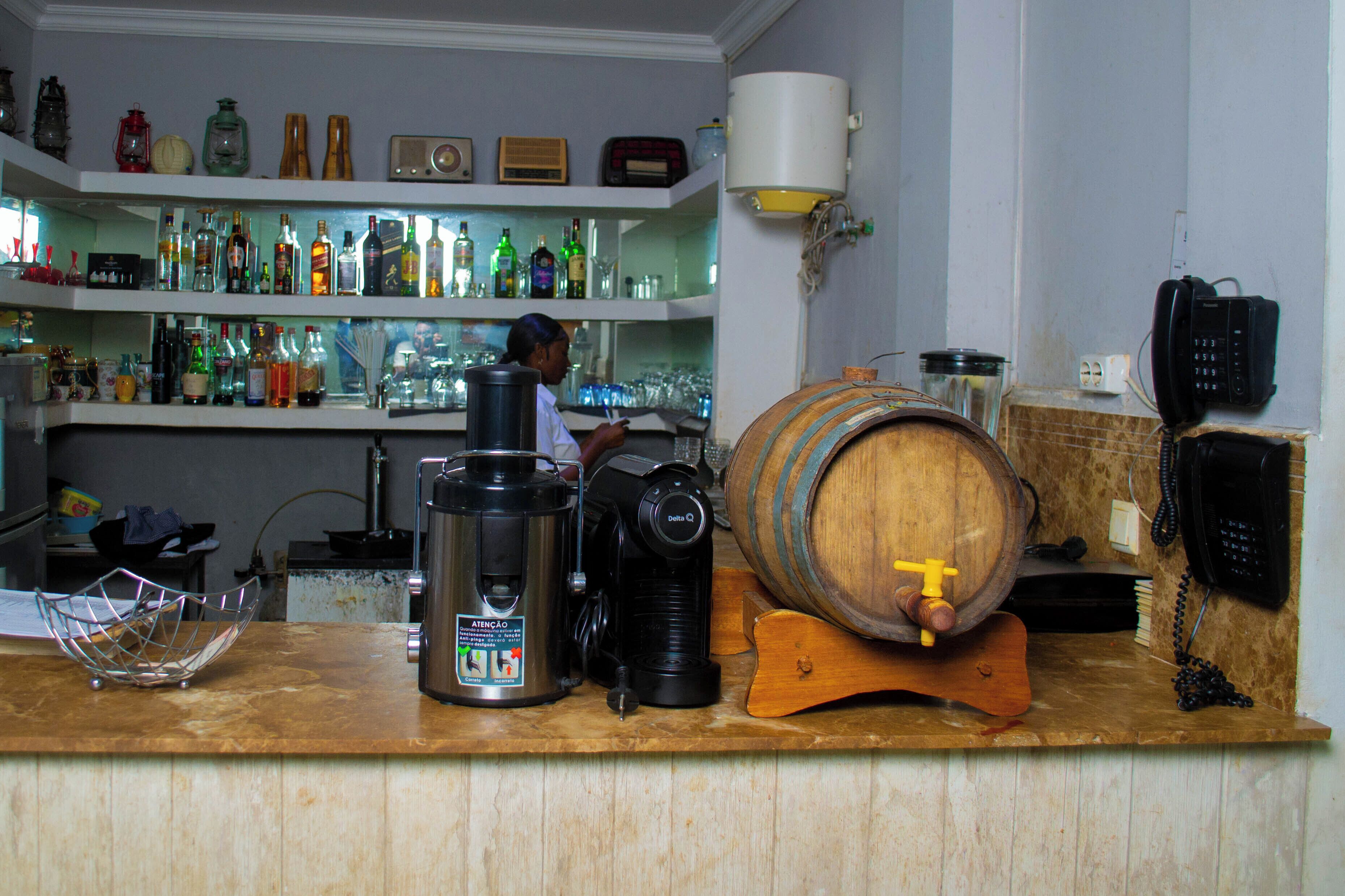 A bar area with shelves of bottles, a coffee machine, a wooden barrel, and a telephone.