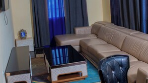 A living room with a sectional sofa, a coffee table, and a TV on a stand. - HOTEL LLAELL (Luanda)