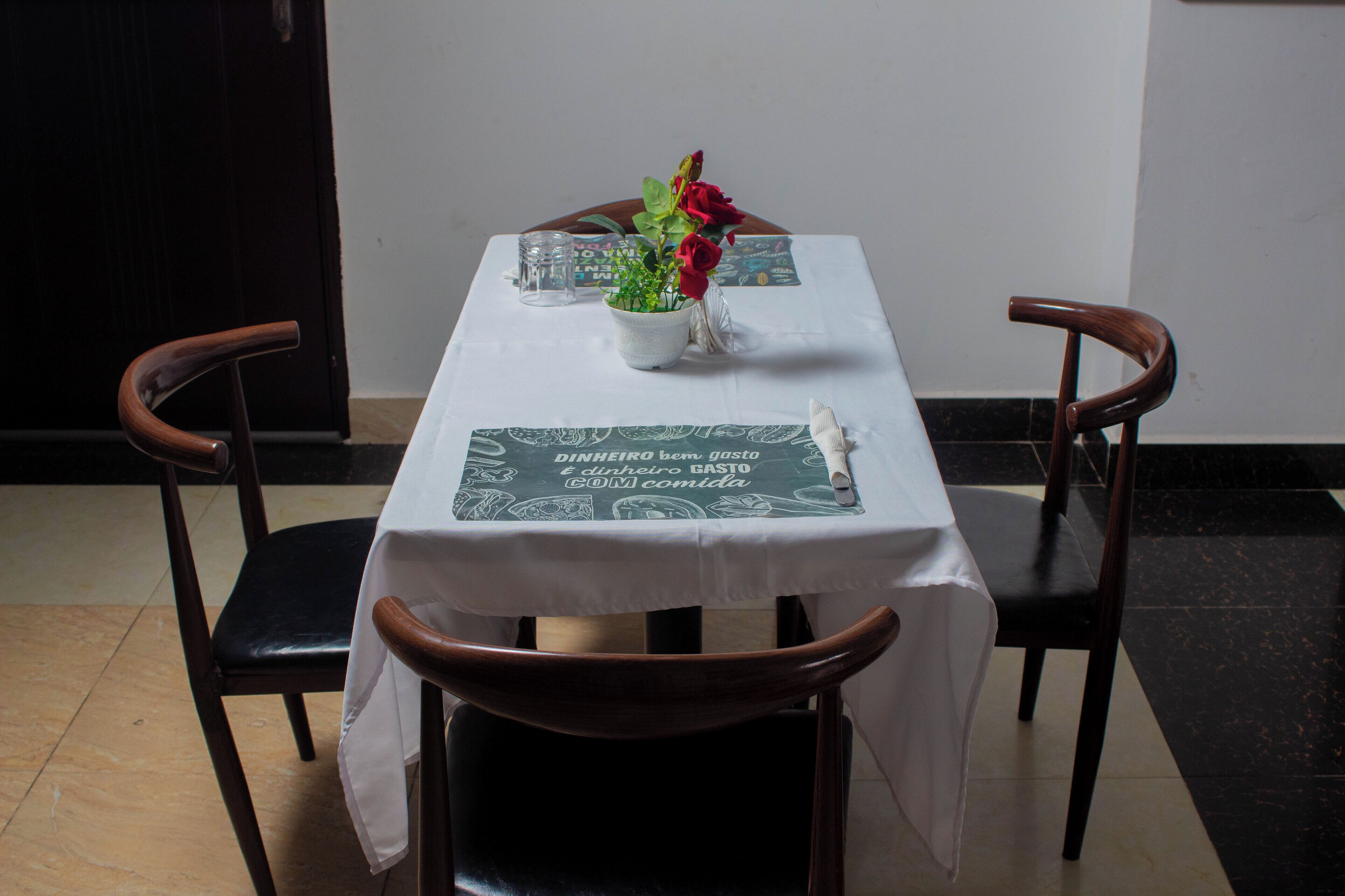 A dining table with a white tablecloth, two wooden chairs, a vase with flowers, and a menu.