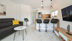Un salon moderne comprenant un canapé, une table basse et des tabourets de bar. Il comprend également un coin cuisine avec un four à micro-ondes, un réfrigérateur et un comptoir-bar.