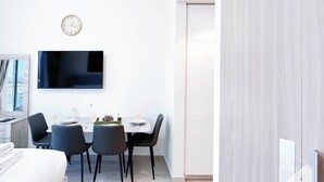 Una habitación de hotel moderna con una cama, un área de comedor con sillas y una mesa, un televisor montado en la pared y un reloj.