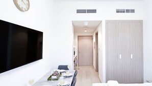 Una habitación de hotel moderna con zona de comedor, televisor de pantalla plana, cama y armario.
