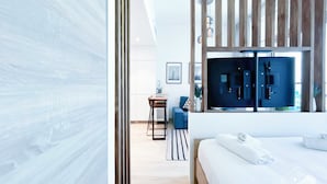 A modern hotel room with a large bed, a wooden partition, a desk with a chair, and a view of the city through large windows. - Balcony Bliss: Cozy Studio With Marina Views (Dubai)