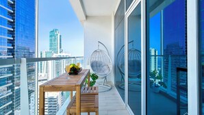 A balcony with a wooden table, two chairs, and a hanging chair. - Balcony Bliss: Cozy Studio With Marina Views (Dubai)