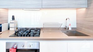 A modern kitchen with a gas stove, oven, and a stainless steel sink. - Balcony Bliss: Cozy Studio With Marina Views (Dubai)