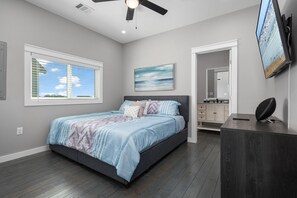 Un dormitorio con cama, ventilador de techo, televisión y ventana con persianas.