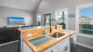 A modern kitchen with a wooden countertop, a stainless steel sink, and a built-in dishwasher. - Villa Brisa Del Mar 2 Bedroom Home (Port Bolivar)