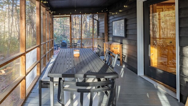 A covered outdoor dining area with a wooden table and chairs, large windows, and a ceiling fan. - Shadows Nest - Unique, Rustic-Modern Design with Local Art (Sautee)