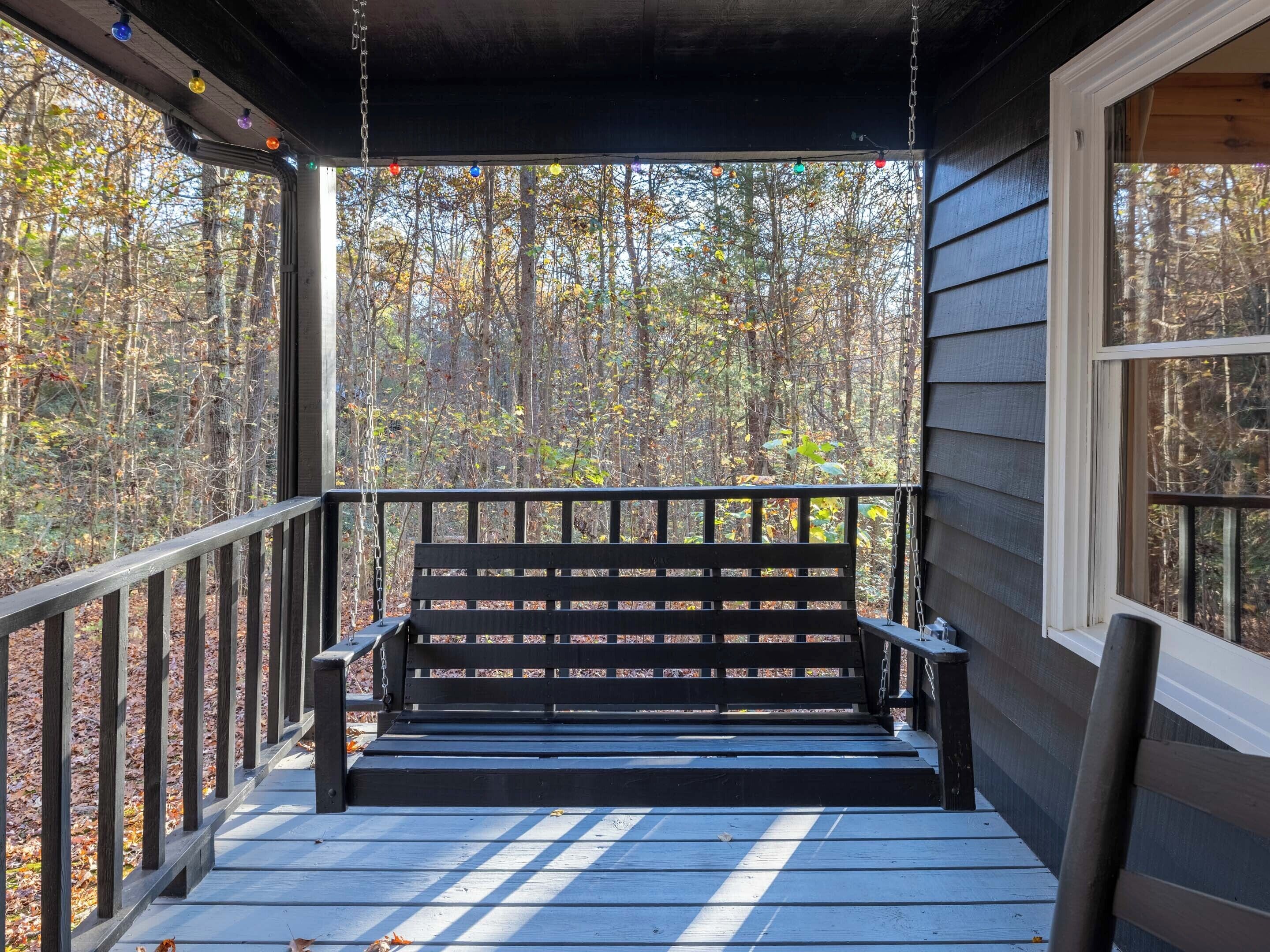 A wooden deck with a black bench, surrounded by a railing, overlooking a forested area.