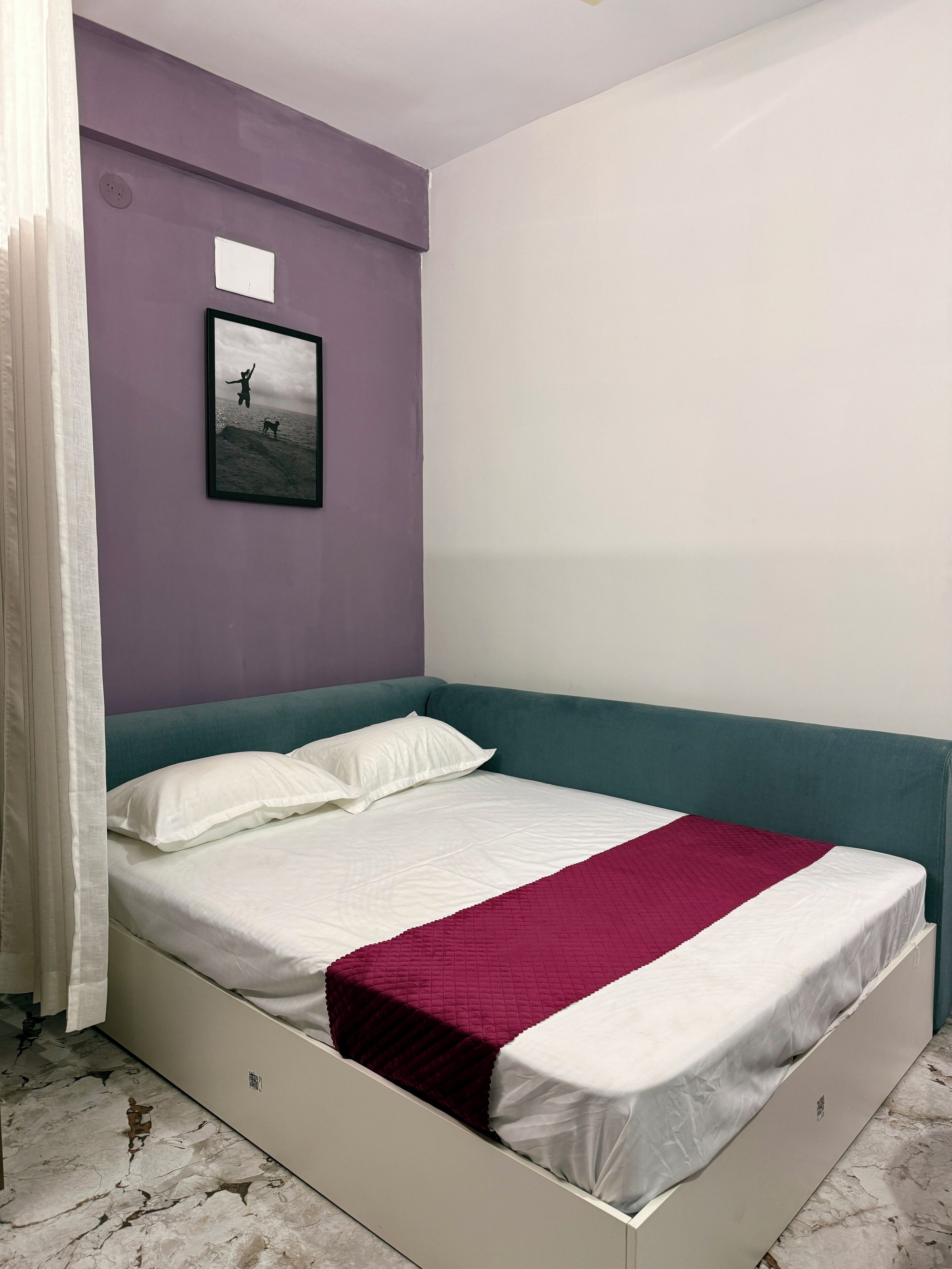 Een slaapkamer met een bed, een paarse wand, een ingelijst beeld en een wit plafond.