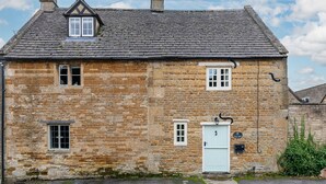 A stone building with a gabled roof, a white door, and a small window with a white frame. - Wyck Cottage - pet friendly in Wyck Rissington near Bourton-on-the-Water (near Bourton-on-the-Water)