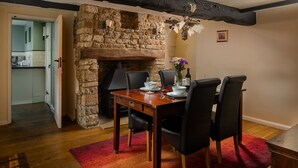 A dining area with a stone fireplace, a table set for four, and a red rug on the floor. - Wyck Cottage - pet friendly in Wyck Rissington near Bourton-on-the-Water (near Bourton-on-the-Water)