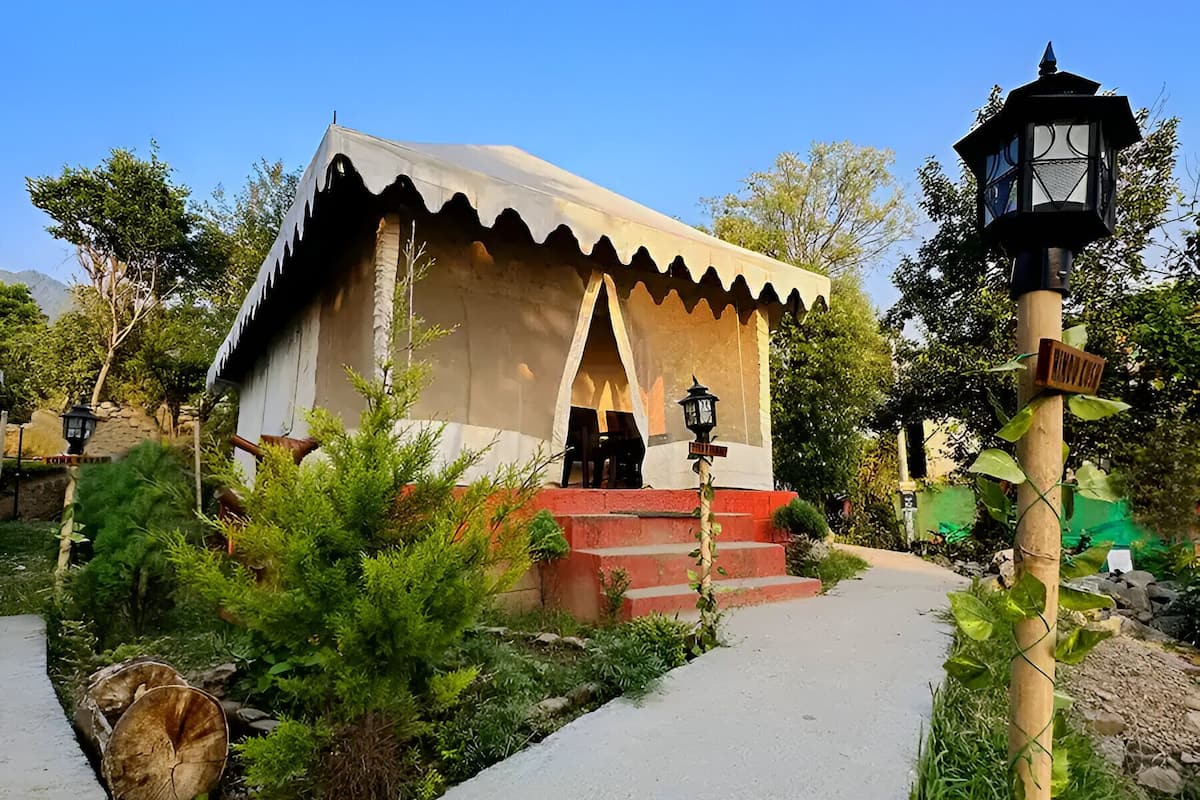Un bâtiment de style traditionnel, en forme de tente, avec un escalier menant à l’entrée, entouré de verdure et bordé d’un chemin pavé.