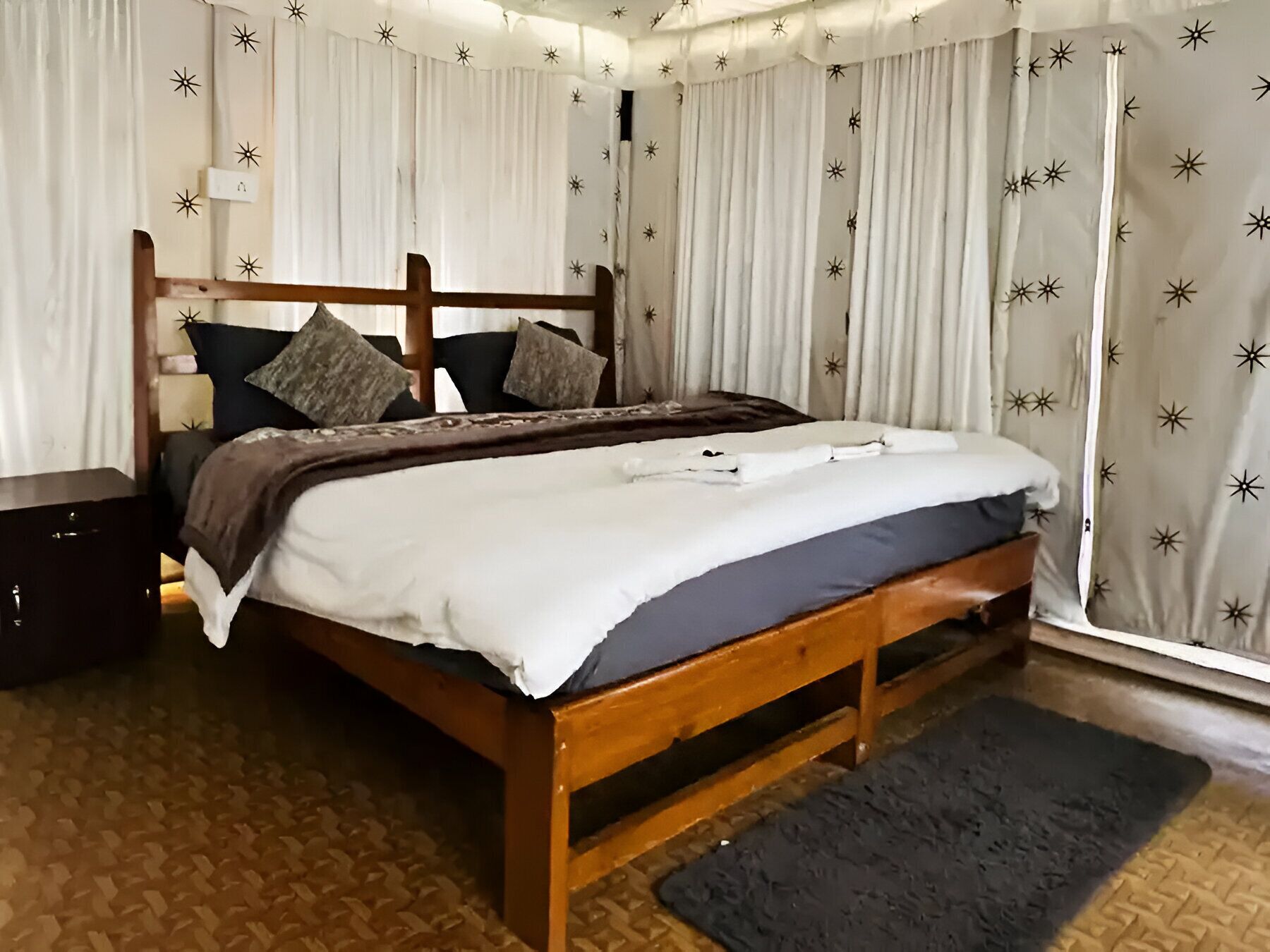 A wooden bed with a white and dark blue bedspread, two pillows, and a bedside table.