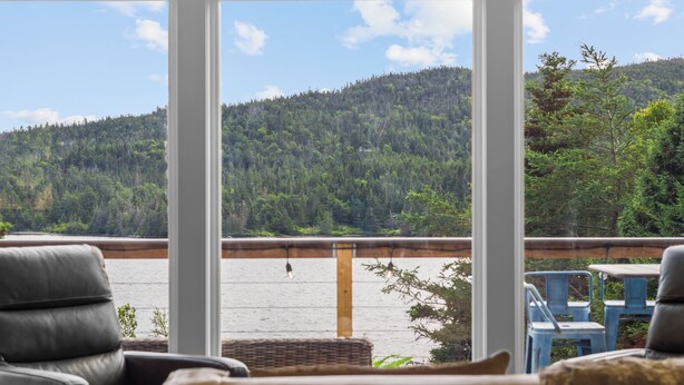 Une pièce avec vue sur un lac et une forêt. On y trouve des chaises et une table près de la fenêtre.