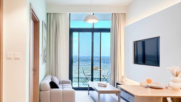 A modern living room with a sofa, a dining table, and a TV. - Luxury 1BR With Balcony in Azizi Riviera (Dubai)