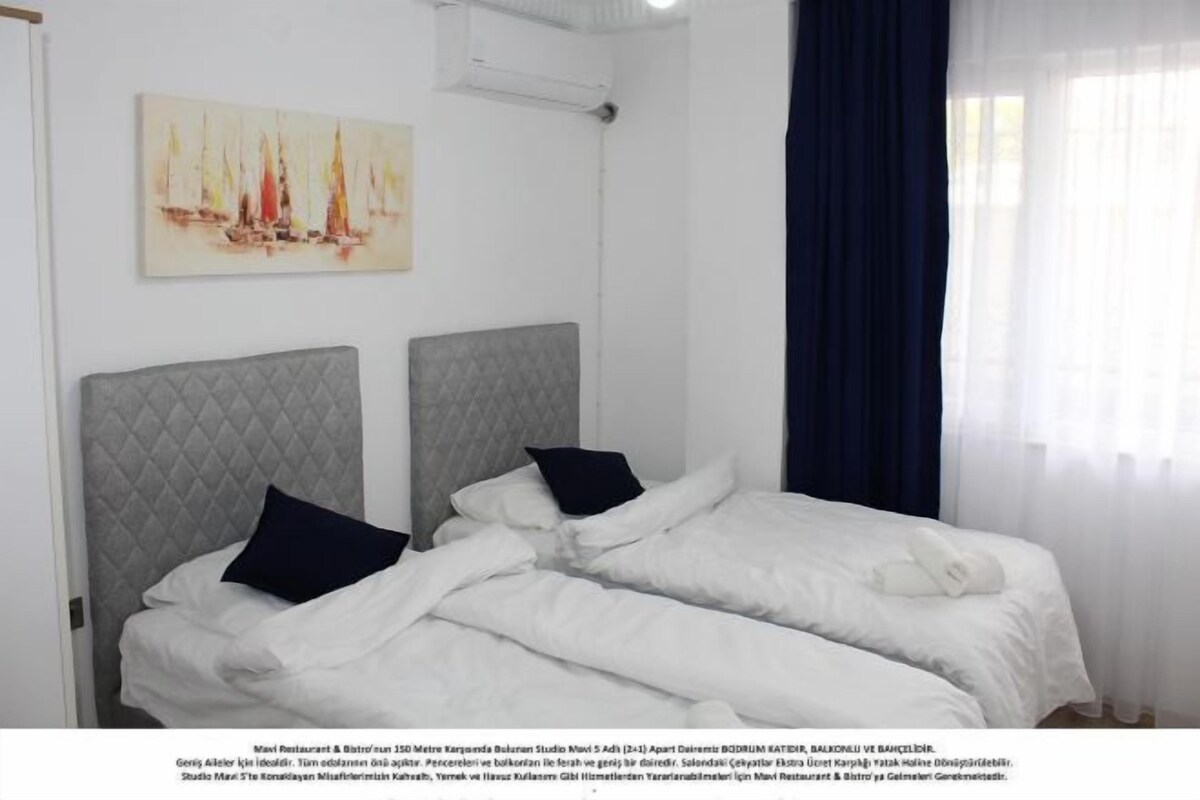 A double bed with a grey headboard, white bedding, and a black pillow.