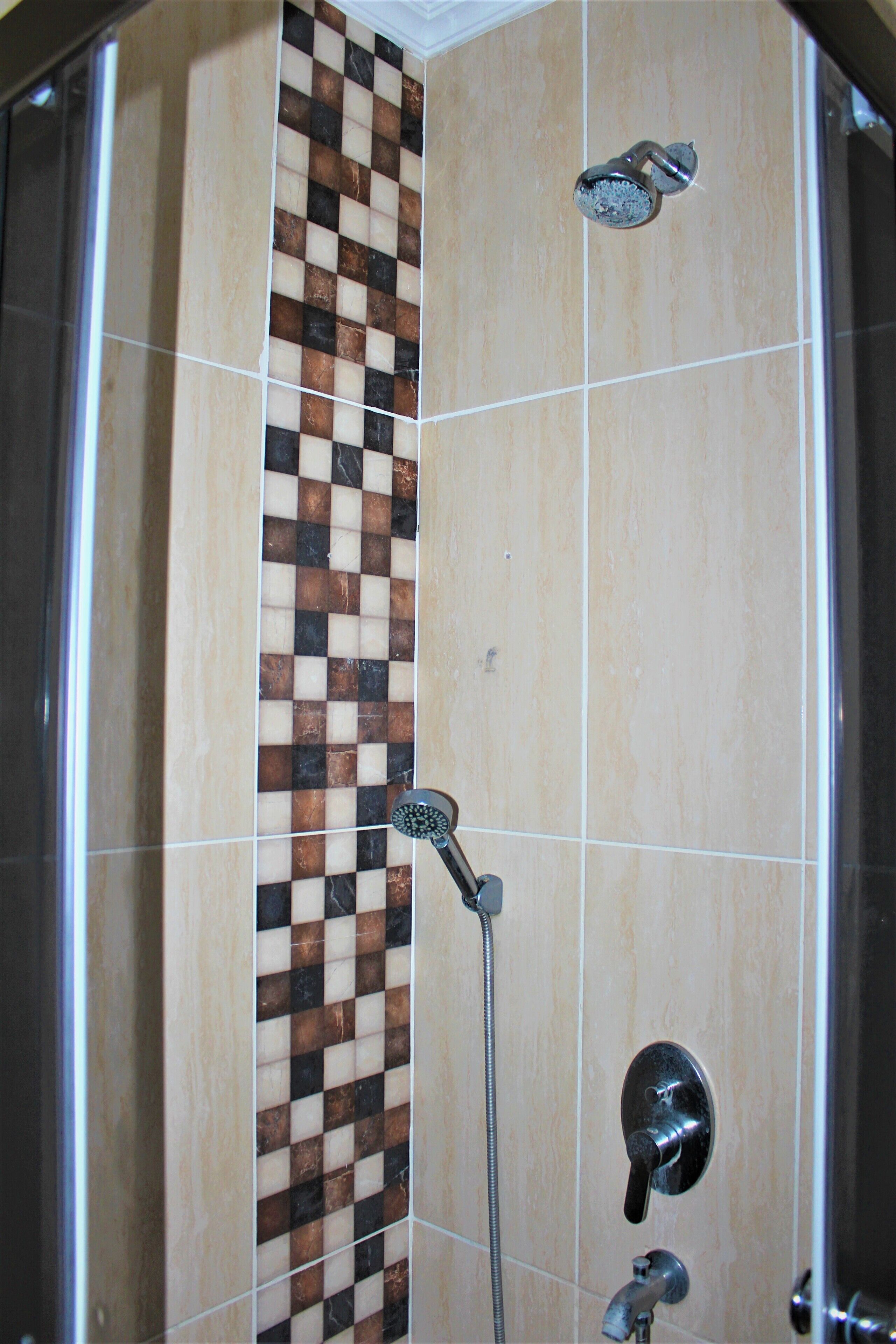 A shower with a checkered tile design, a handheld showerhead, and a wall-mounted faucet.