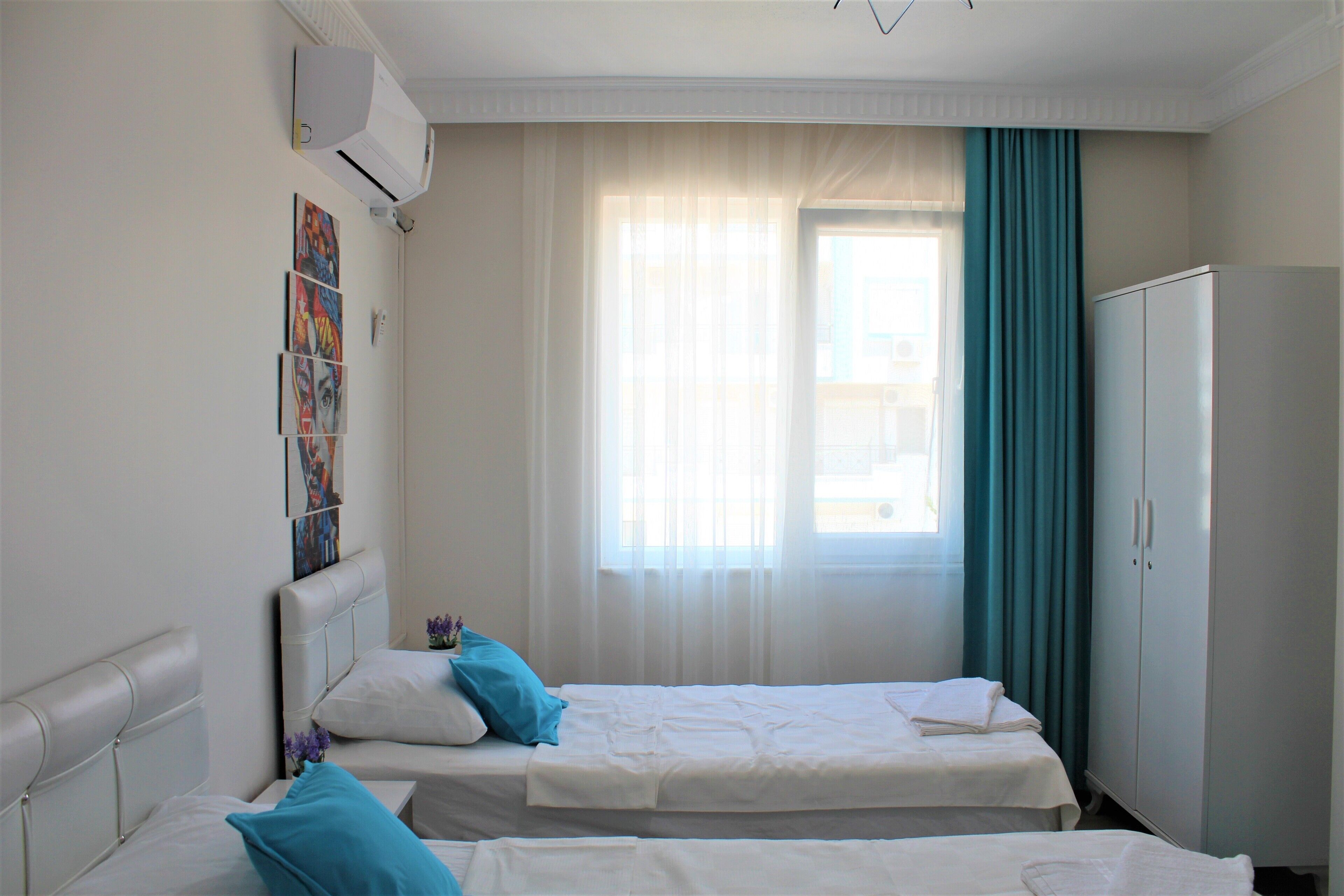 A hotel room with two beds, a wardrobe, and a window with sheer curtains.