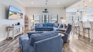 Ein geräumiges Wohnzimmer mit einem großen, blauen Ecksofa, einem Holztisch und einem Essbereich mit weißem Tisch und Stühlen.