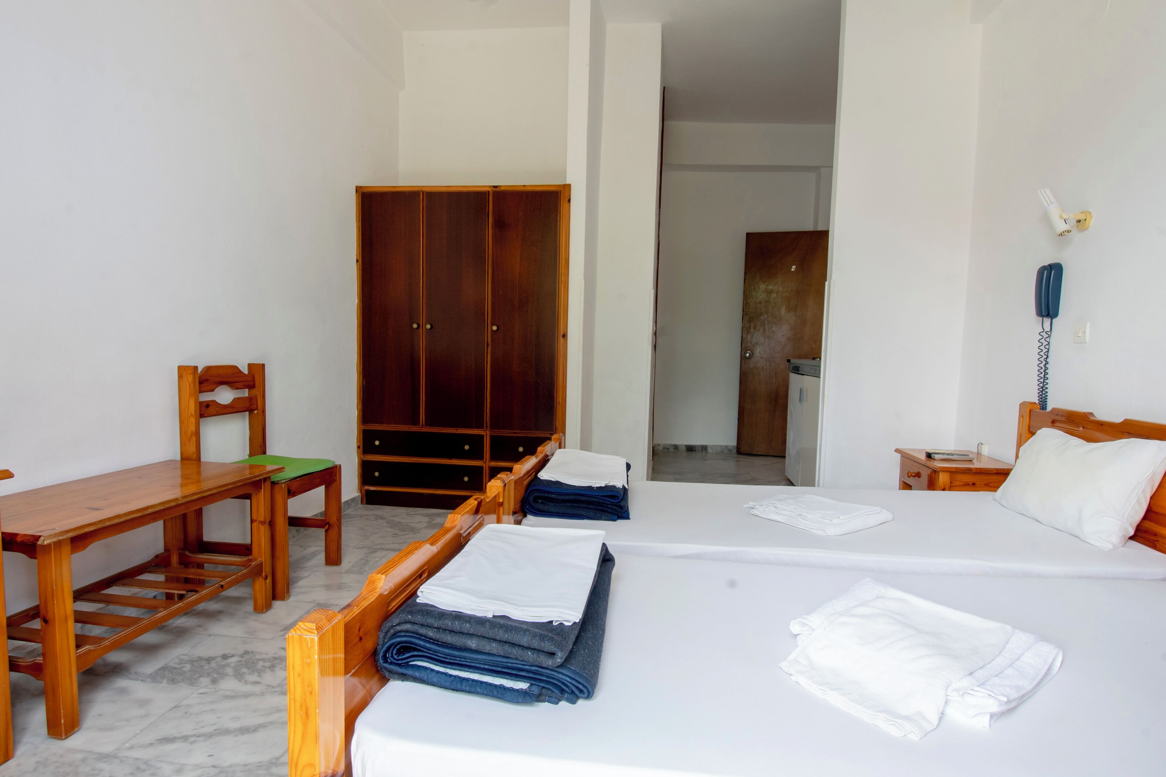 Una habitación de hotel con cama, escritorio de madera, silla, armario y baño visible a través de una puerta abierta.