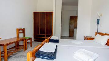 Una habitación de hotel con cama, escritorio de madera, silla, armario y baño visible a través de una puerta abierta.