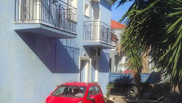A red car parked in a cobblestone courtyard with a blue building featuring balconies and a red-tiled roof.