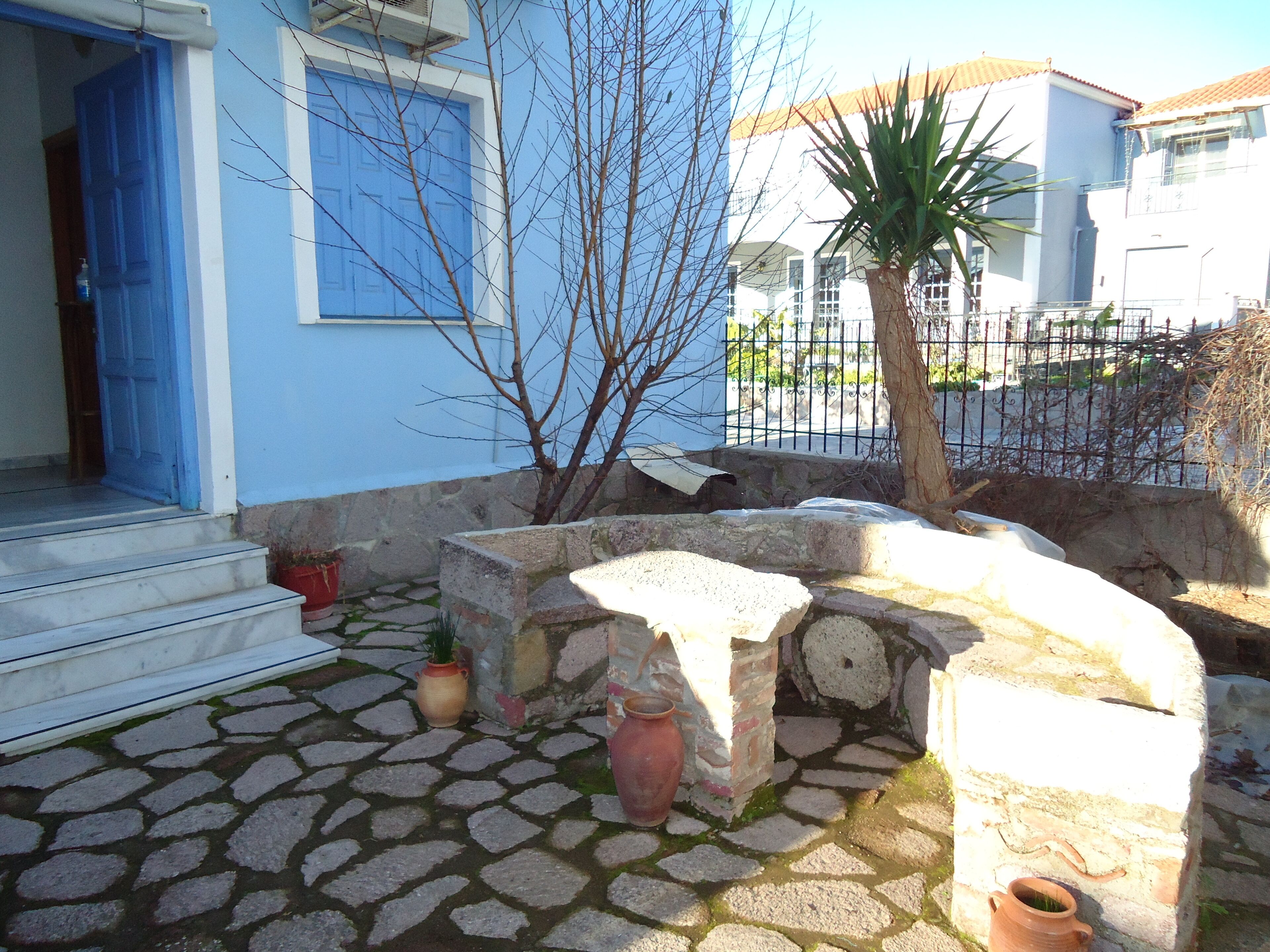 Un patio empedrado con puerta azul, plantas en macetas y un banco de piedra.