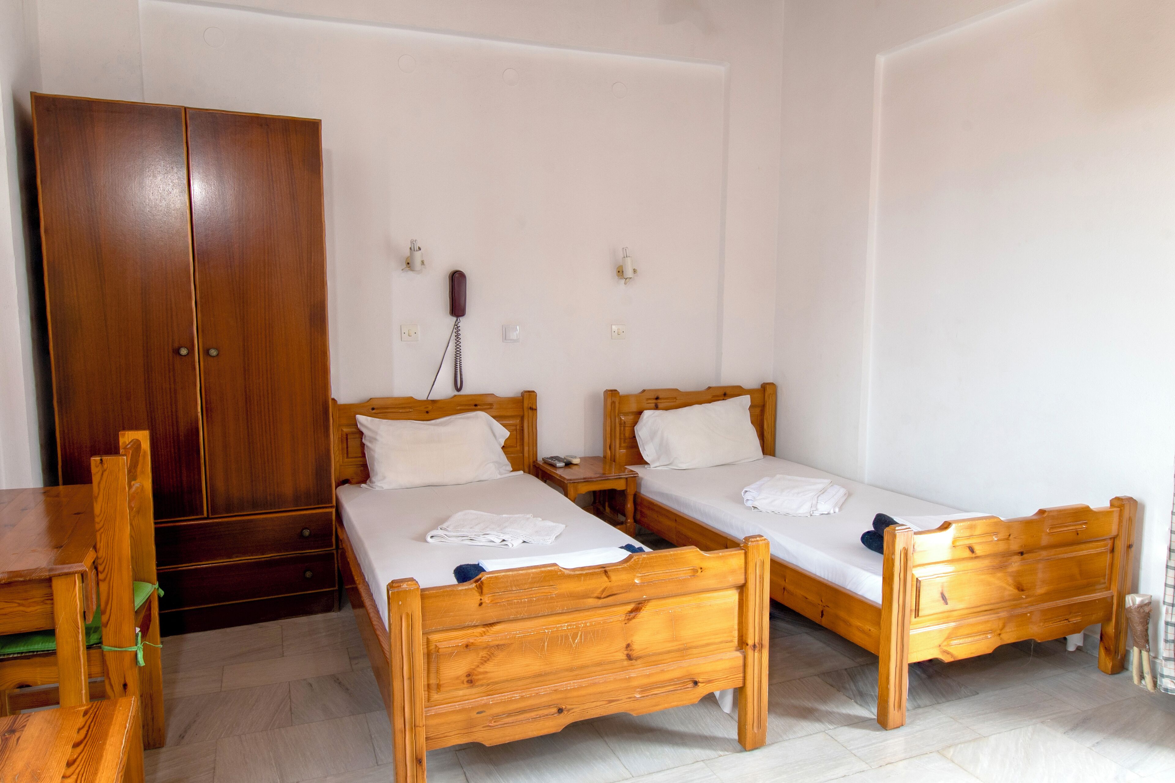 A room with two wooden beds, a wooden wardrobe, a wooden table, and a telephone on the wall.