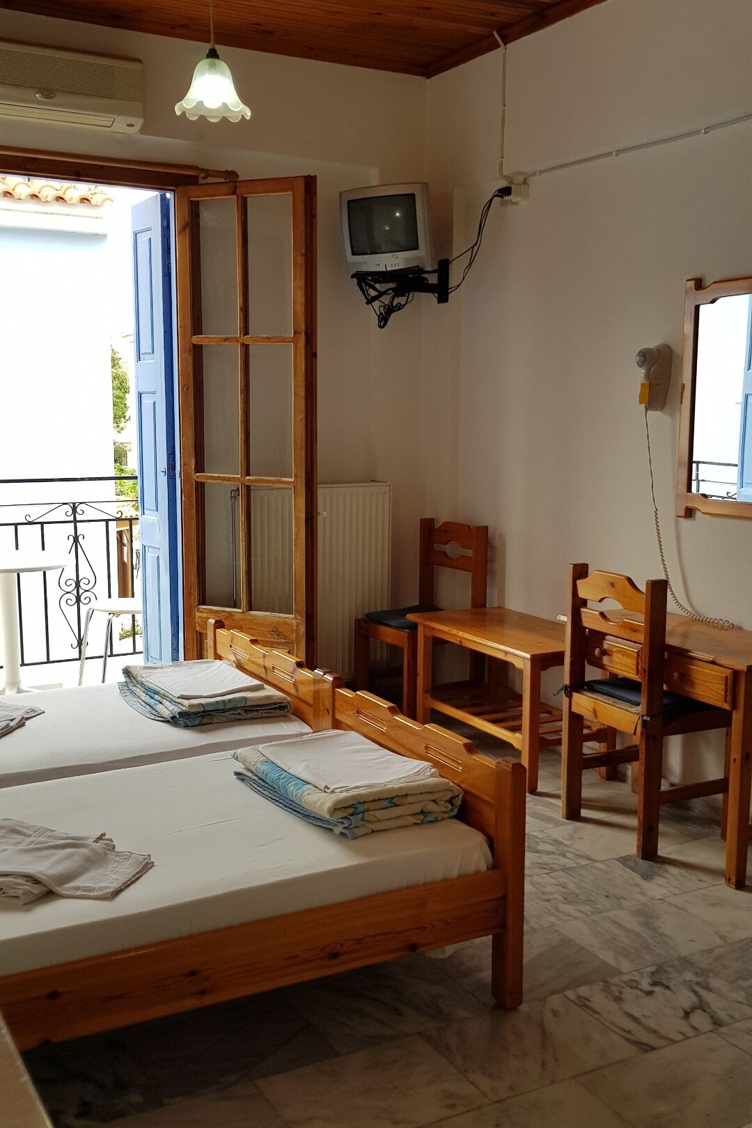 A room with two wooden beds, a small table, a chair, a television, and a radiator.