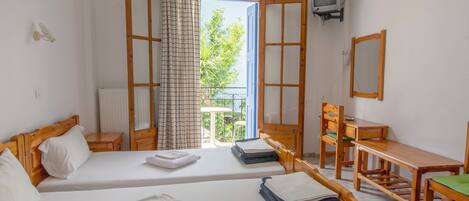 A room with two beds, a desk, a chair, a television, and a window with a view of greenery.