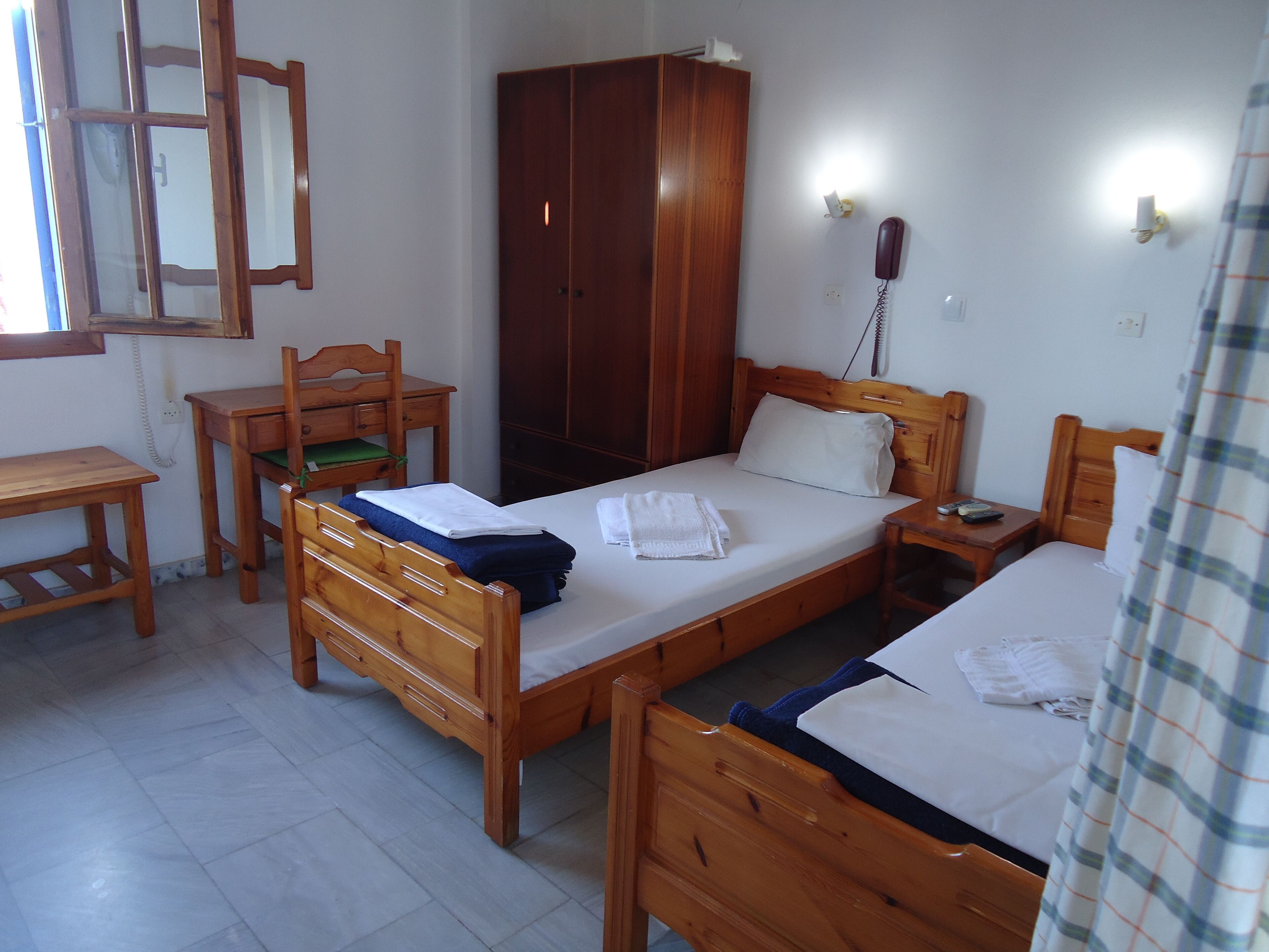 Una habitación con dos camas de madera, un escritorio de madera, una silla, un armario y un espejo.