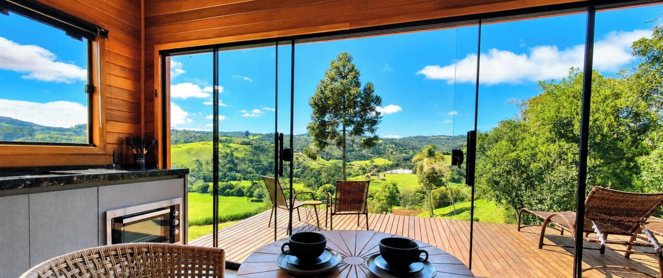 Una terraza de madera con una mesa y sillas, con vistas a un paisaje exuberante con colinas y árboles.