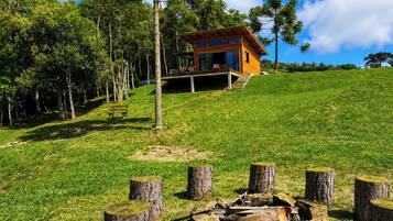 A modern wooden cabin on a grassy hill with a clear sky.