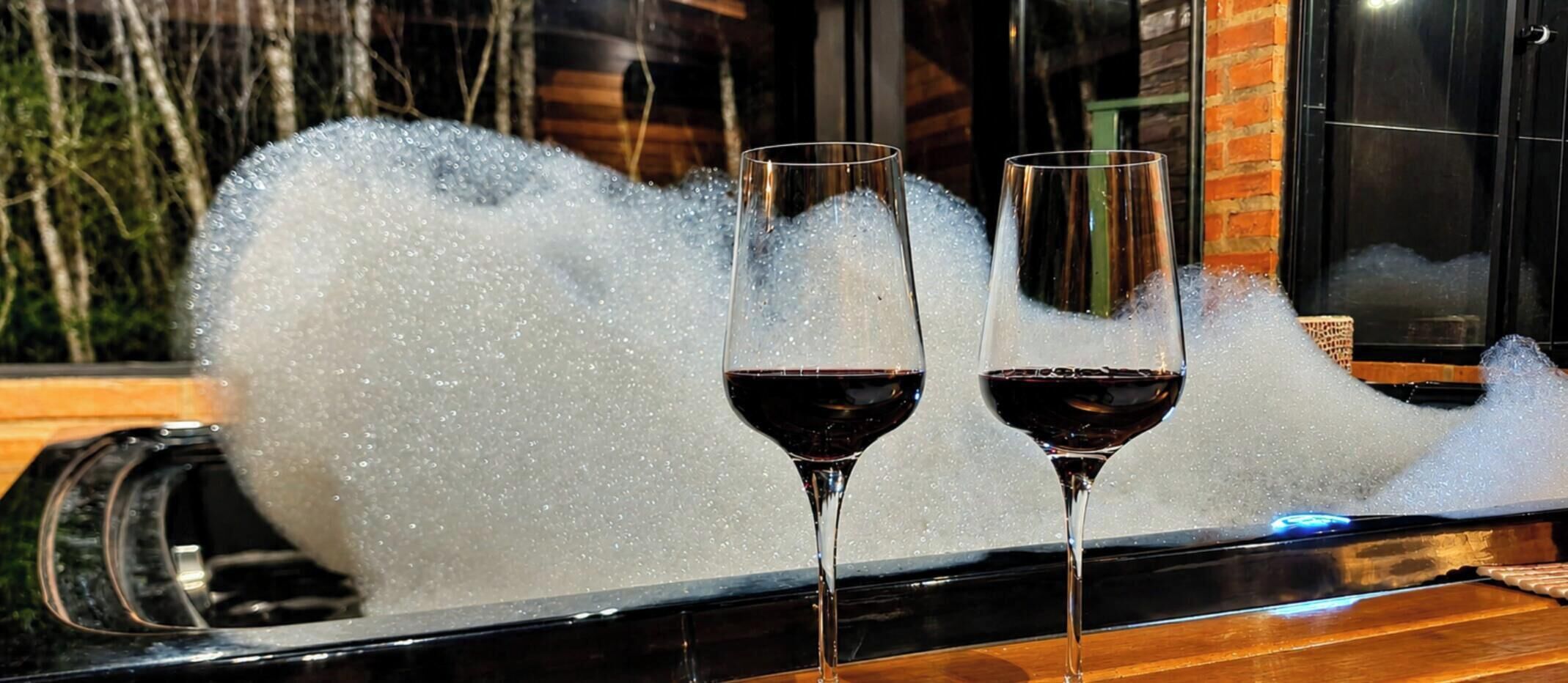 Two glasses of red wine on a tray with a foamy liquid behind them.