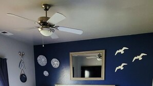 Ein Schlafzimmer mit Bett, Nachttisch, Deckenventilator und Wanddekorationen.