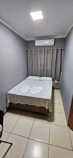 A small, neatly arranged bedroom with a bed, an air conditioning unit, and a curtain. - Hotel Itaverá ll (Presidente Prudente)