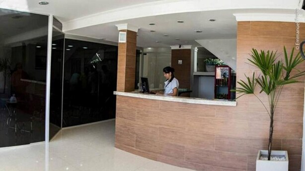 Zona de recepción con recepcionista, mostrador, planta en maceta y pared de vidrio.