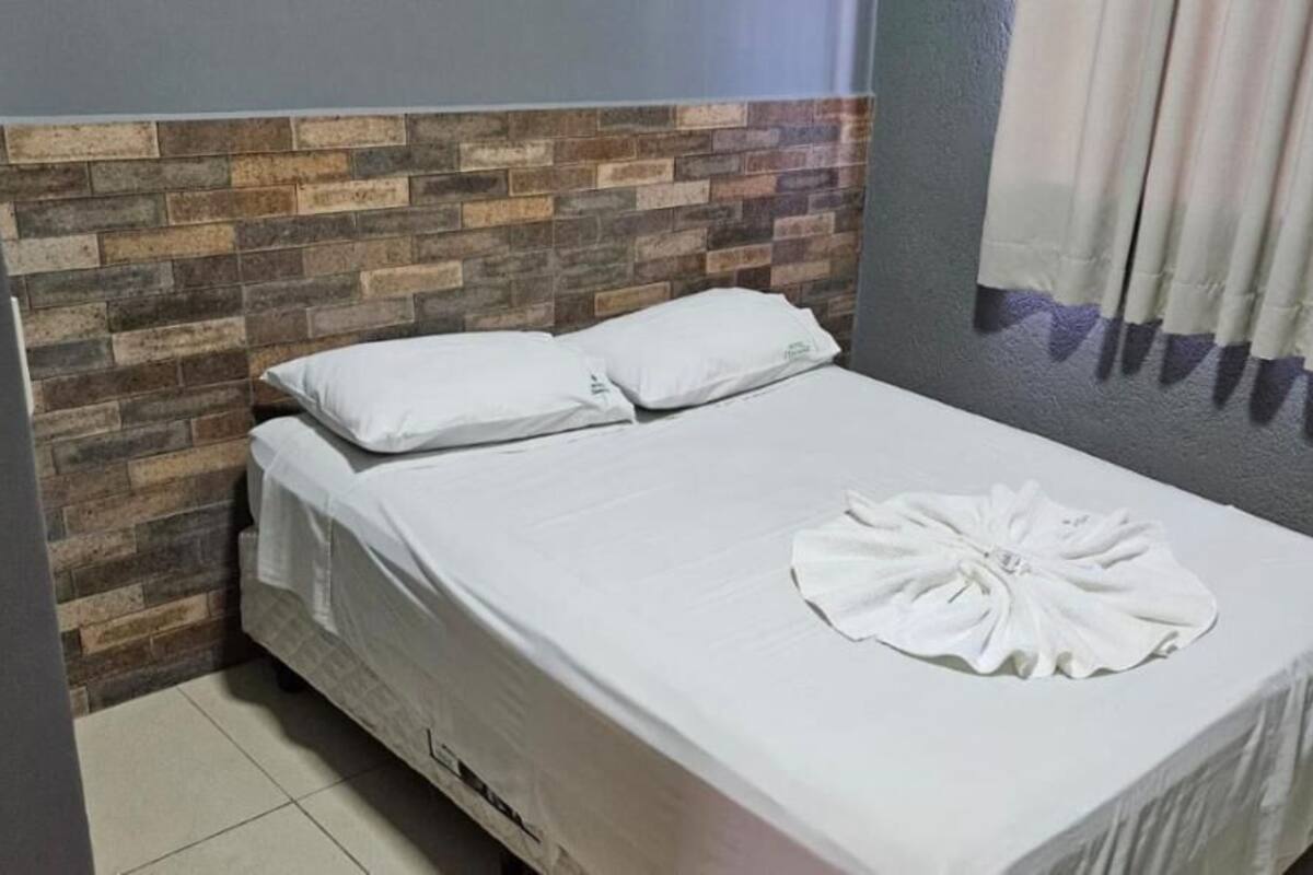 Una cama bien hecha con sábanas blancas y una toalla doblada sobre ella.