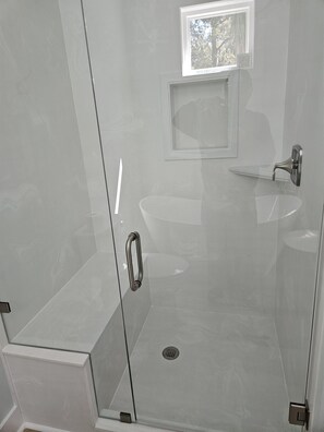 A modern bathroom with a glass-enclosed shower, a sink, and a small window. - The Seashelle is a New Four Bedroom, Four ½ Bath home with a Pool. (Fripp Island)