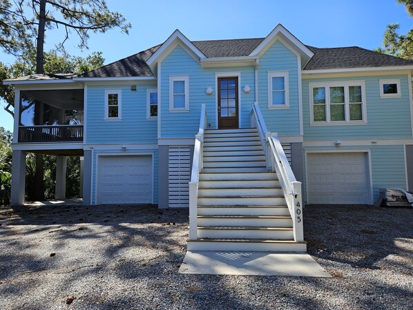 A two-story house with a front porch, a staircase leading to the front door, and a garage. - The Seashelle is a New Four Bedroom, Four ½ Bath home with a Pool. (Fripp Island)