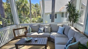A covered outdoor seating area with a wooden deck, a beige sectional sofa, and a small table. - The Seashelle is a New Four Bedroom, Four ½ Bath home with a Pool. (Fripp Island)