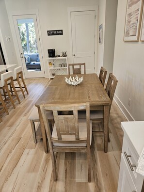 A dining area with a wooden table and chairs, a coffee bar sign, and a door leading outside. - The Seashelle is a New Four Bedroom, Four ½ Bath home with a Pool. (Fripp Island)