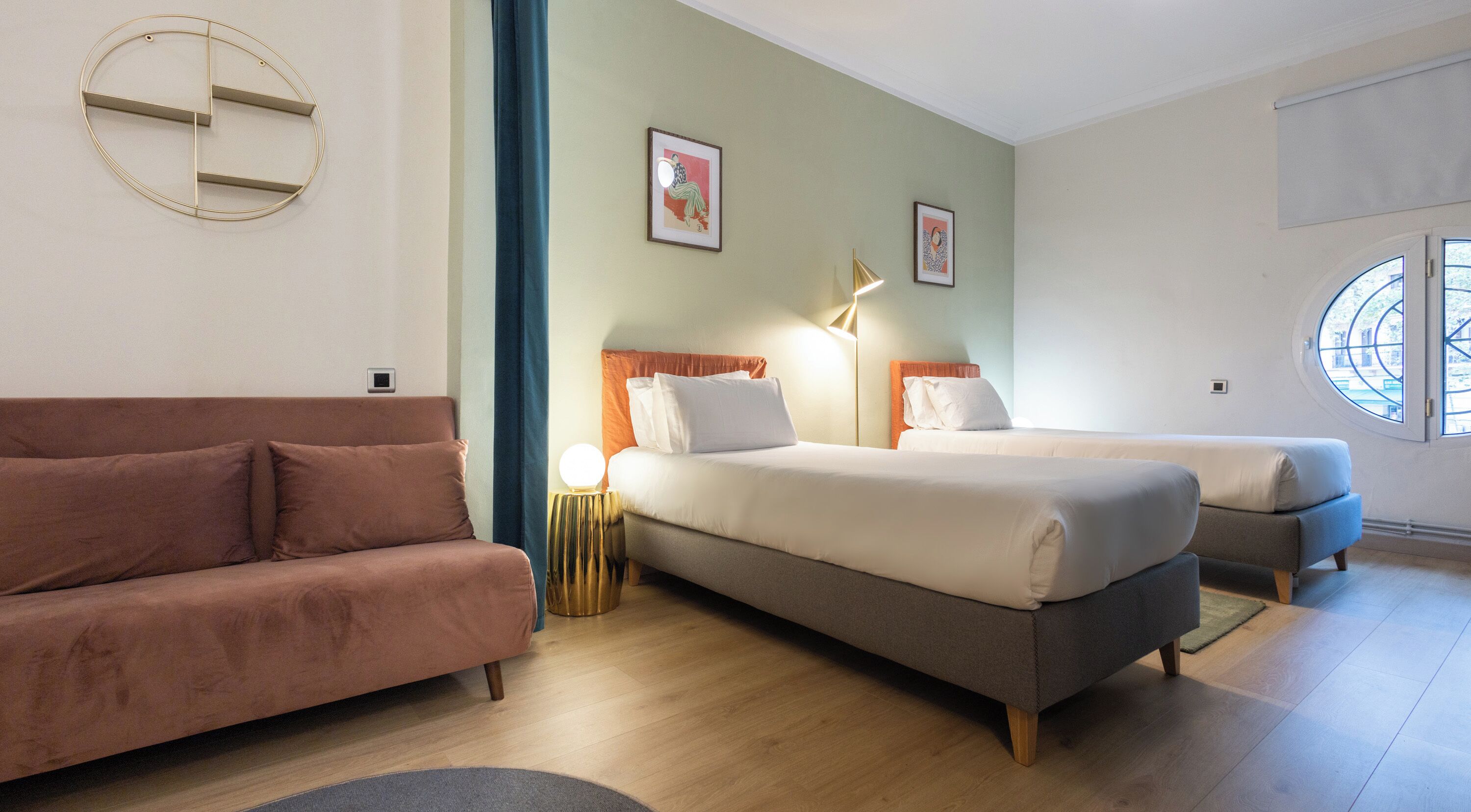 A hotel room with two beds, a sofa, a round wall decoration, and a window with a view.