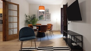A dining area with a round table, orange chairs, a blue chair, a black TV on the wall, a plant, and a black and white rug. - Stay U-nique Apartment Gran Via IV (Barcelona)